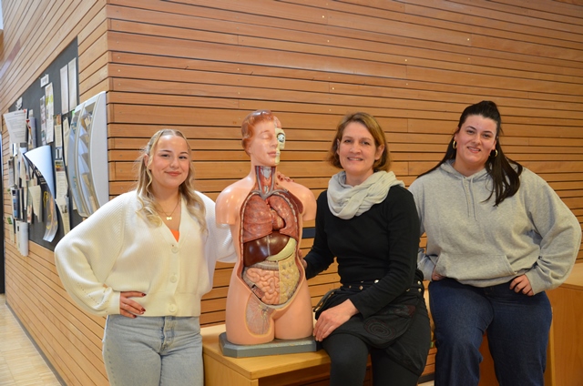 Zwei angehende Heilerziehungspflegerinnen und die Leiterin der Fachschule für Heilerziehungspflege der Ludwig Schlaich Akademie stehen am Modell eines menschlichen Oberkörpers.