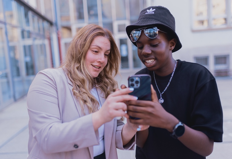 Zwei Personen stehen nebeneinander und schauen in ein Smartphone. 