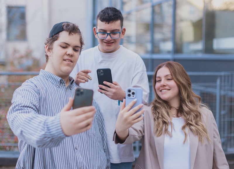 Drei Personen stehen nebeneinander und schauen auf Smartphones.  