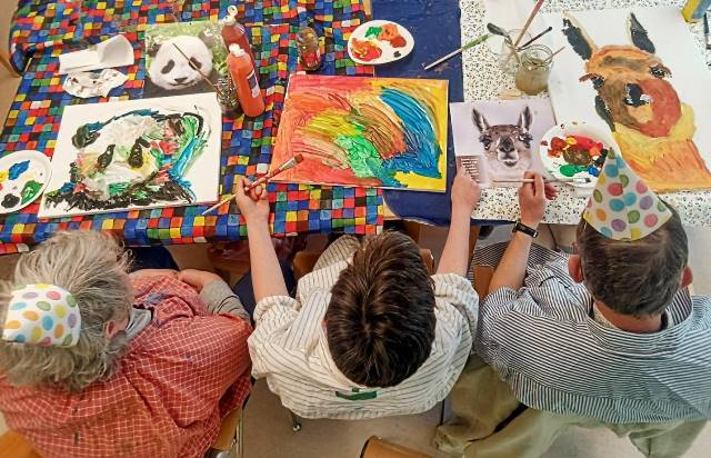 Drei Personen sitzen an einem Tisch und malen Tierbilder. Drei Personen sitzen an einem Tisch und malen Tierbilder.