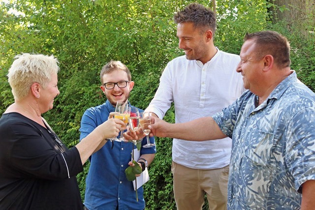 Vier Personen stehen beieinander und stoßen mit gefüllten Gläsern auf den Erfolg der Ausbildung an. 