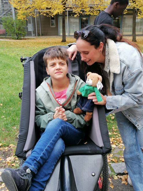 Eine Person übergibt einen der Hoffnungsbären an ein Kind der Kindergruppe im Wildermuthhaus (KiWi), das in einem Rollstuhl sitzt. Eine Person übergibt einen der Hoffnungsbären an ein Kind der Kindergruppe im Wildermuthhaus (KiWi), das in einem Rollstuhl sitzt.