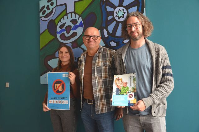 Nebeneinander stehen drei Mitarbeitende, die zusammen mit weiteren Mitarbeitenden aus dem Arbeitskreis das neue „Gewaltschutzkonzept“ überarbeitet haben.