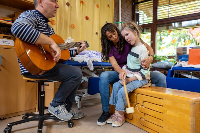 Mit Musik regen zwei Sonderpädagogen die Sinne einer Schülerin an. Eine Person spielt Gitarre. Mit Musik regen zwei Sonderpädagogen die Sinne einer Schülerin an. Eine Person spielt Gitarre.