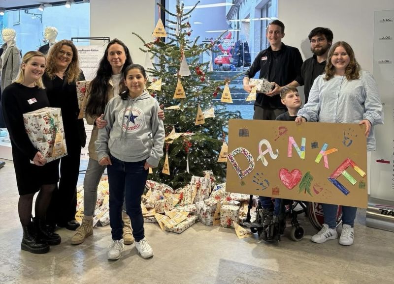 Mehrere Personen stehen am Wunschbaum aus dem Jahr 2025, zwei Personen halten vor sich ein Plakat mit dem Wort Danke in bunten Buchstaben. Mehrere Personen stehen am Wunschbaum aus dem Jahr 2025, zwei Personen halten vor sich ein Plakat mit dem Wort Danke in bunten Buchstaben.
