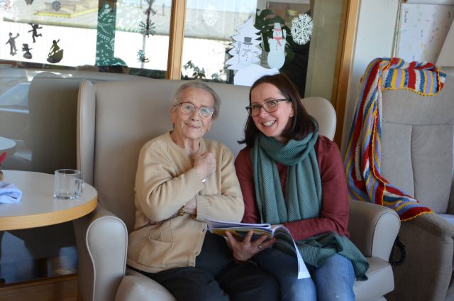 Zwei Personen sitzen nebeneinander und blicken lächelnd Richtung Kamera.