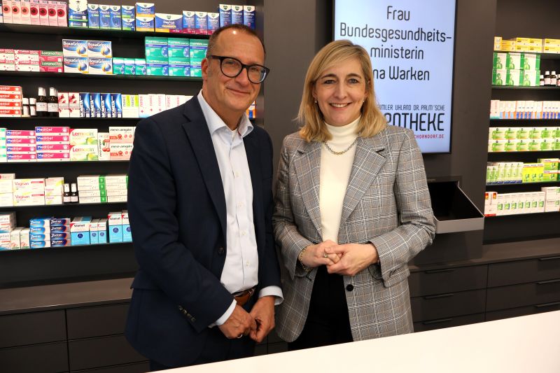 Der Vorstandsvorsitzende der Diakonie Stetten und die Bundesgesundheitsministerin stehen nebeneinander vor einem Regal in der Daimler-Apotheke Schorndorf.  