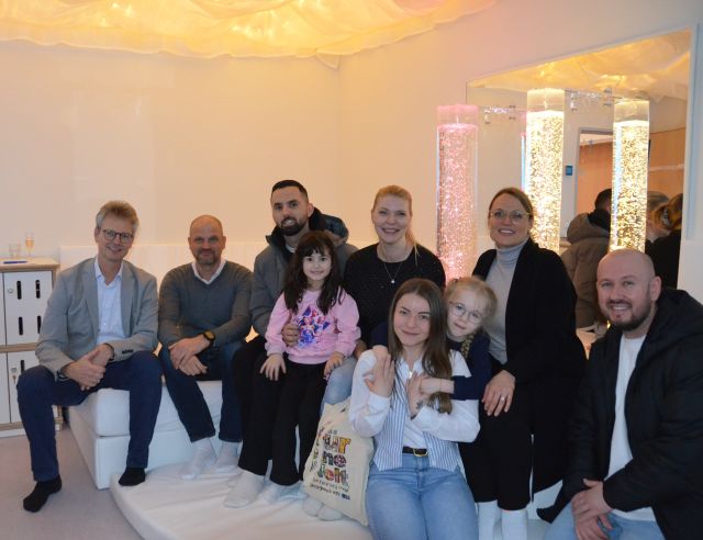 Mitarbeitende, Kinder und Eltern sitzen nebeneinander im neuen Snoezelenraum und lächeln Richtung Kamera.