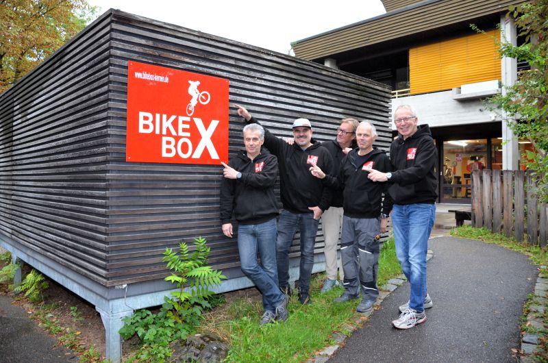 Mehrere Ehrenamtliche der BikeBox zeigen auf ein Schild BikeBox auf dem Schlossberg.  