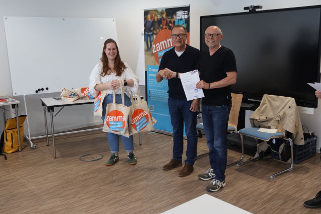 Von links: Die Kursleiterin trägt Stofftaschen mit der Aufschrift „zamma“, der Vorstandsvorsitzende der Diakonie Stetten gratuliert einem Teilnehmer, der sein Zertifikat in den Händen hält. Von links: Die Kursleiterin trägt Stofftaschen mit der Aufschrift „zamma“, der Vorstandsvorsitzende der Diakonie Stetten gratuliert einem Teilnehmer, der sein Zertifikat in den Händen hält.
