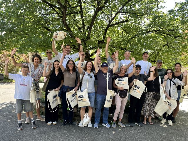 Teilnehmende am SchaffTag – Gruppenfoto vor einem Baum, einige Personen heben die Arme Teilnehmende am SchaffTag – Gruppenfoto vor einem Baum, einige Personen heben die Arme