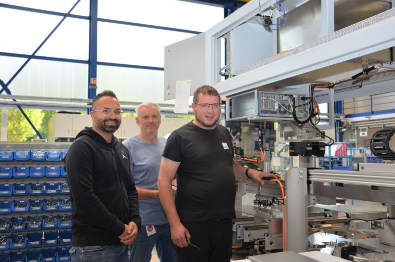 Drei Personen stehen nebeneinander in einer Werkstatt.