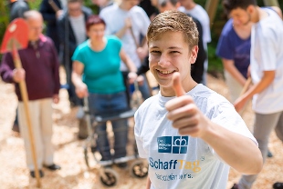 Eine Person mit weißem SchaffTag-Shirt hebt lachend den Daumen